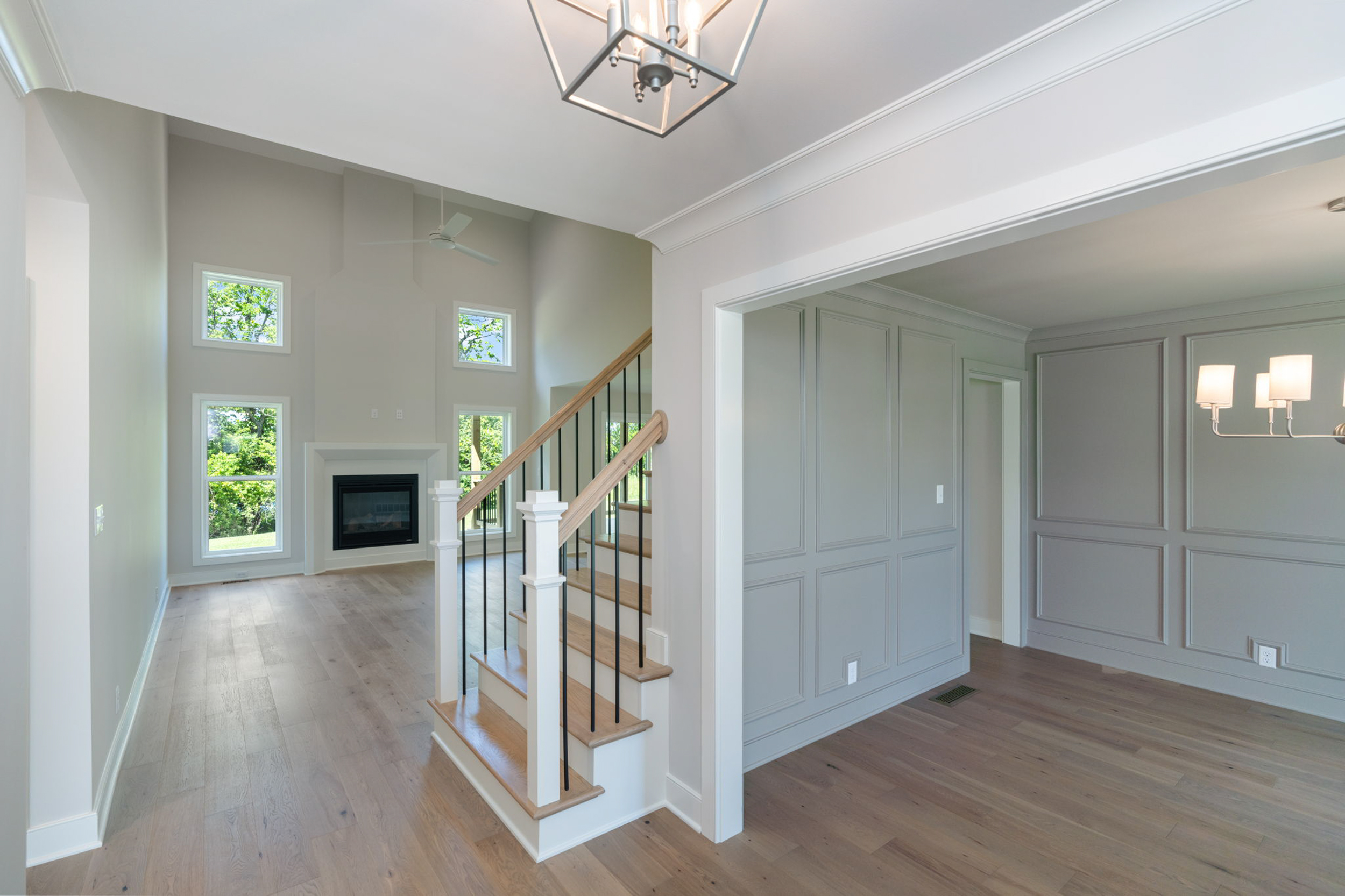 Bright living area with stairs, tall windows, and light-gray paneled walls
