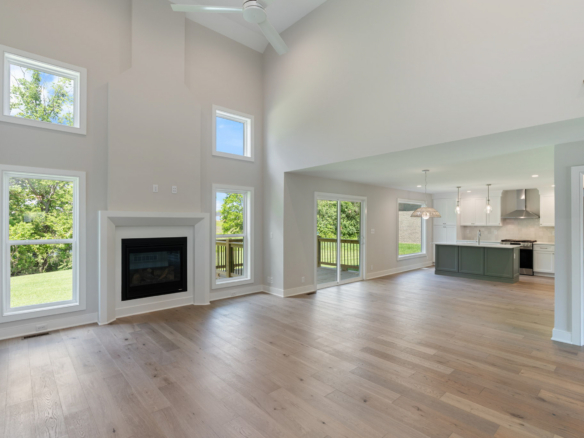Open living area with vaulted ceiling, large windows, a white-framed fireplace, and a kitchen island in the background. (Open-concept space)