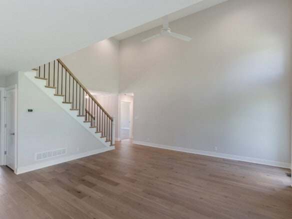 Spacious, empty living room with high ceilings, hardwood floors, and staircase.