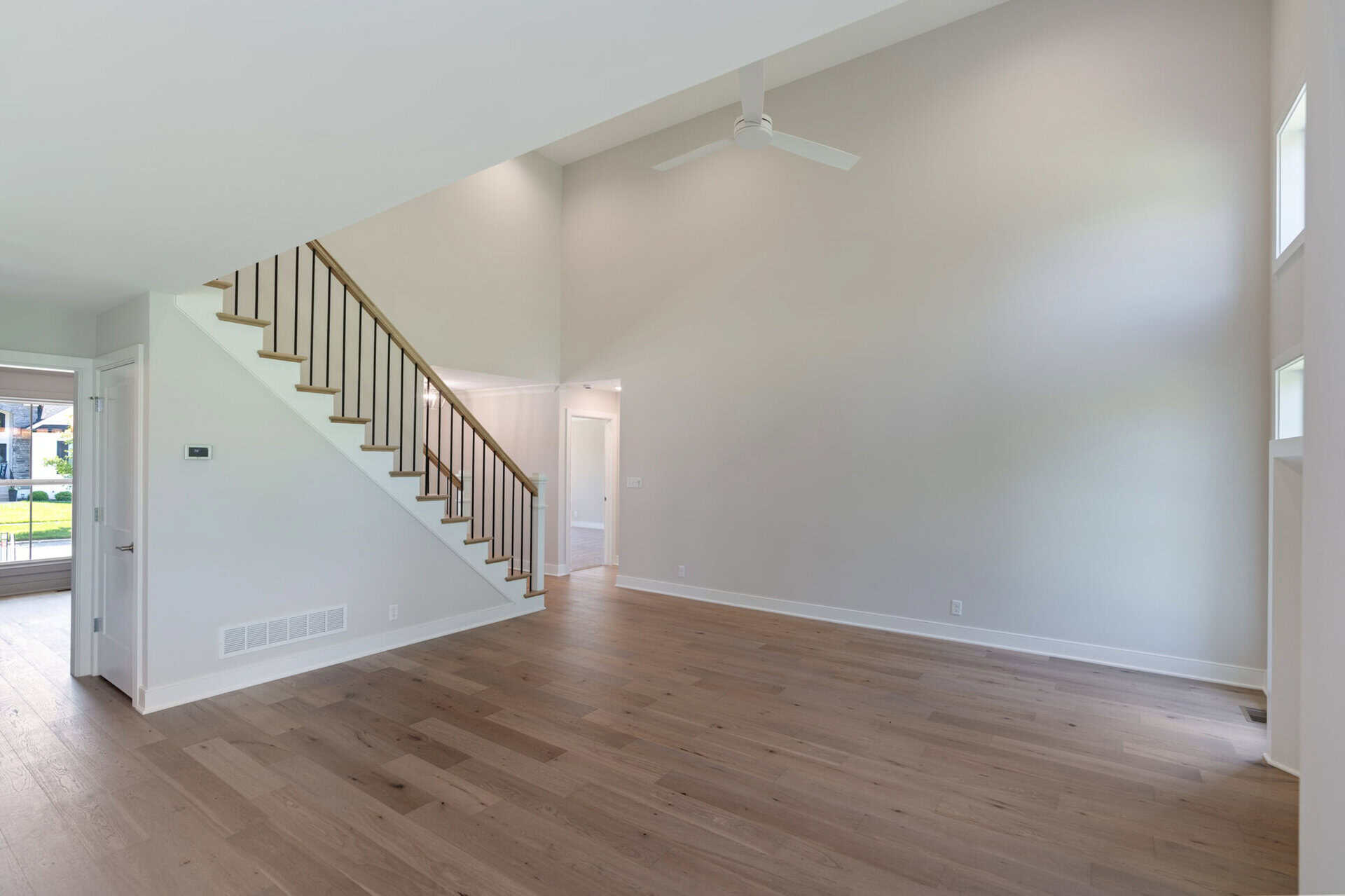 Spacious, empty living room with high ceilings, hardwood floors, and staircase.