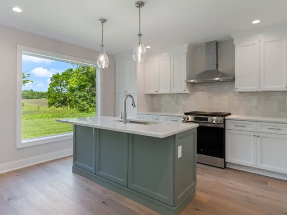 Modern kitchen with white cabinets, gray island, and large window overlooking green landscape.