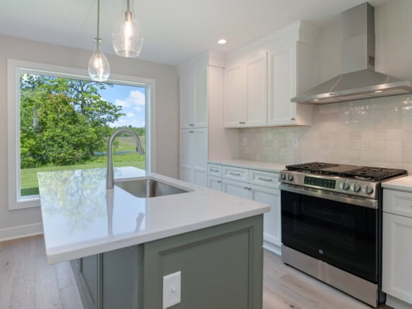 Modern kitchen with white cabinets, stainless steel stove, and large window showing greenery.