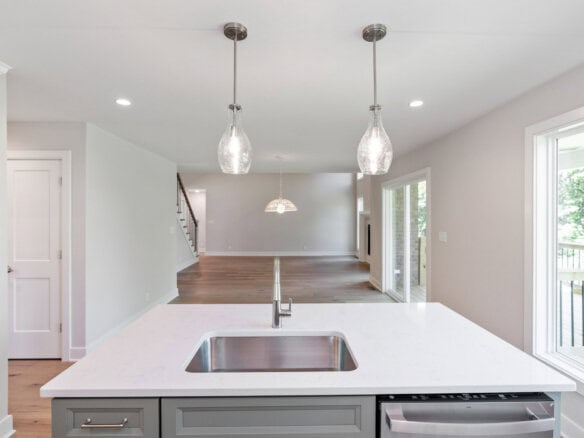 Modern kitchen with white countertops, pendant lights, and large window view.