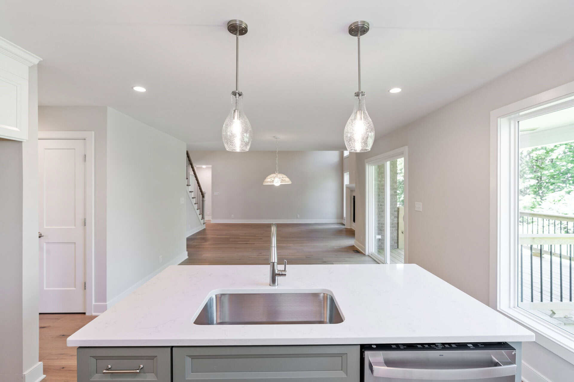 Modern kitchen with white countertops, pendant lights, and large window view.