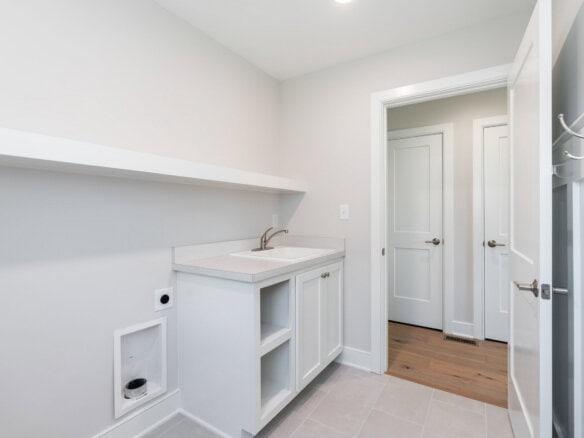 Empty laundry room with white cabinets and a small sink in a new home.