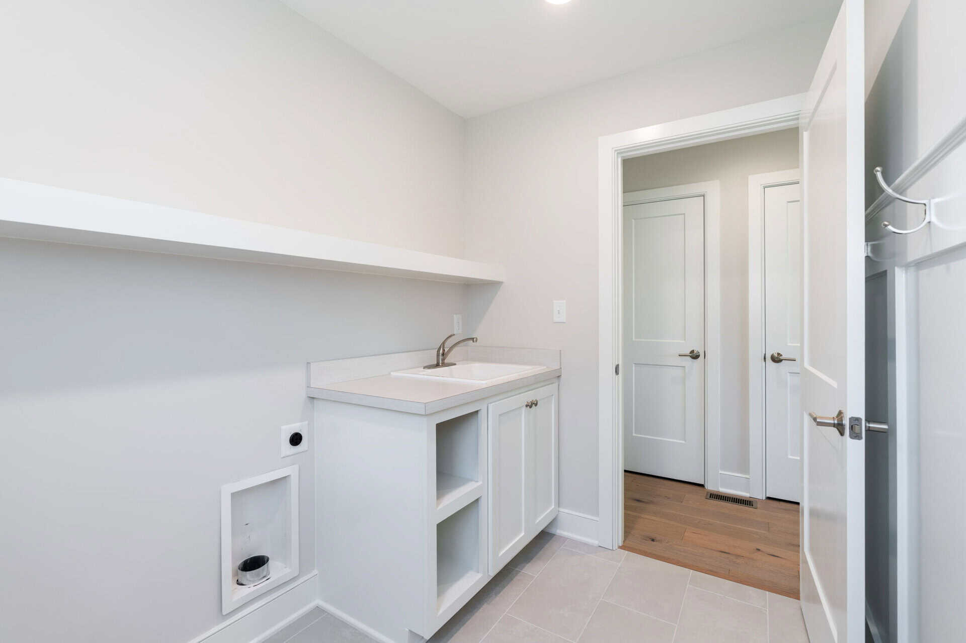 Empty laundry room with white cabinets and a small sink in a new home.