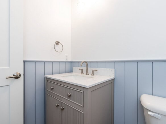 Bathroom vanity with gray cabinet, white countertop, and brass fixtures.