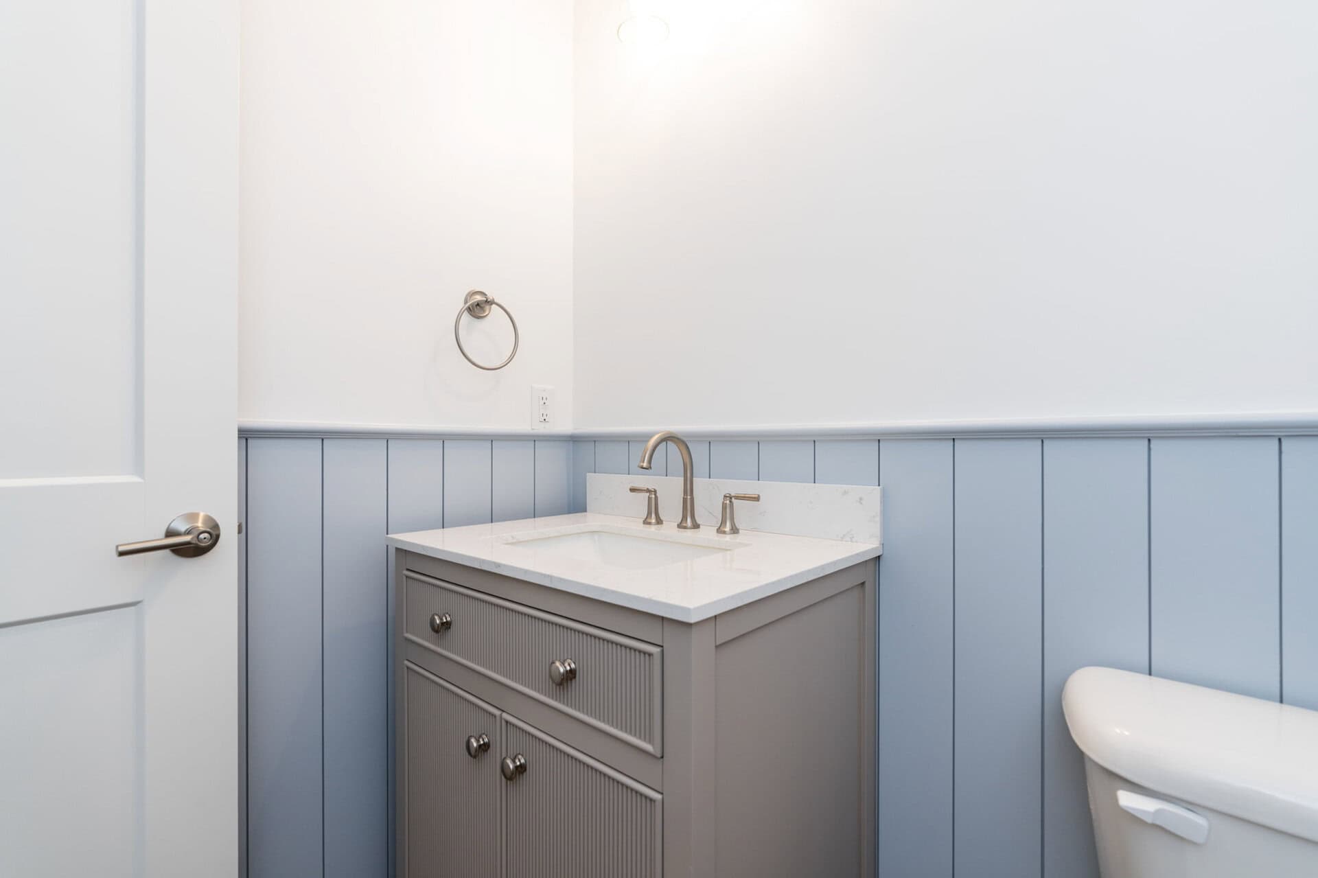 Bathroom vanity with gray cabinet, white countertop, and brass fixtures.