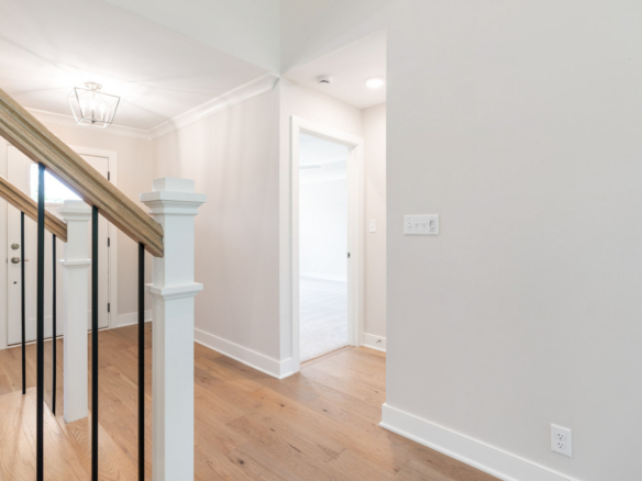 Interior hallway with a wooden staircase and black metal balusters, bright lighting, and light gray walls.