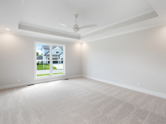 Bright empty bedroom with beige carpet, white ceiling fan, and a large window letting in natural light from outside the home.] ,