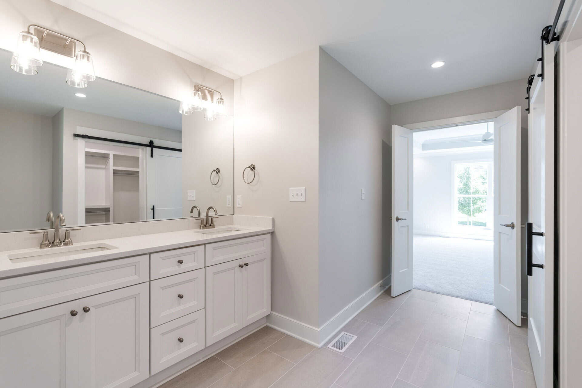Modern bathroom with double vanity and bright adjacent room.