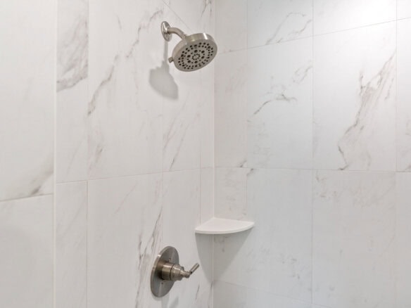 Close-up of a modern shower with marble tiles and a corner shelf.