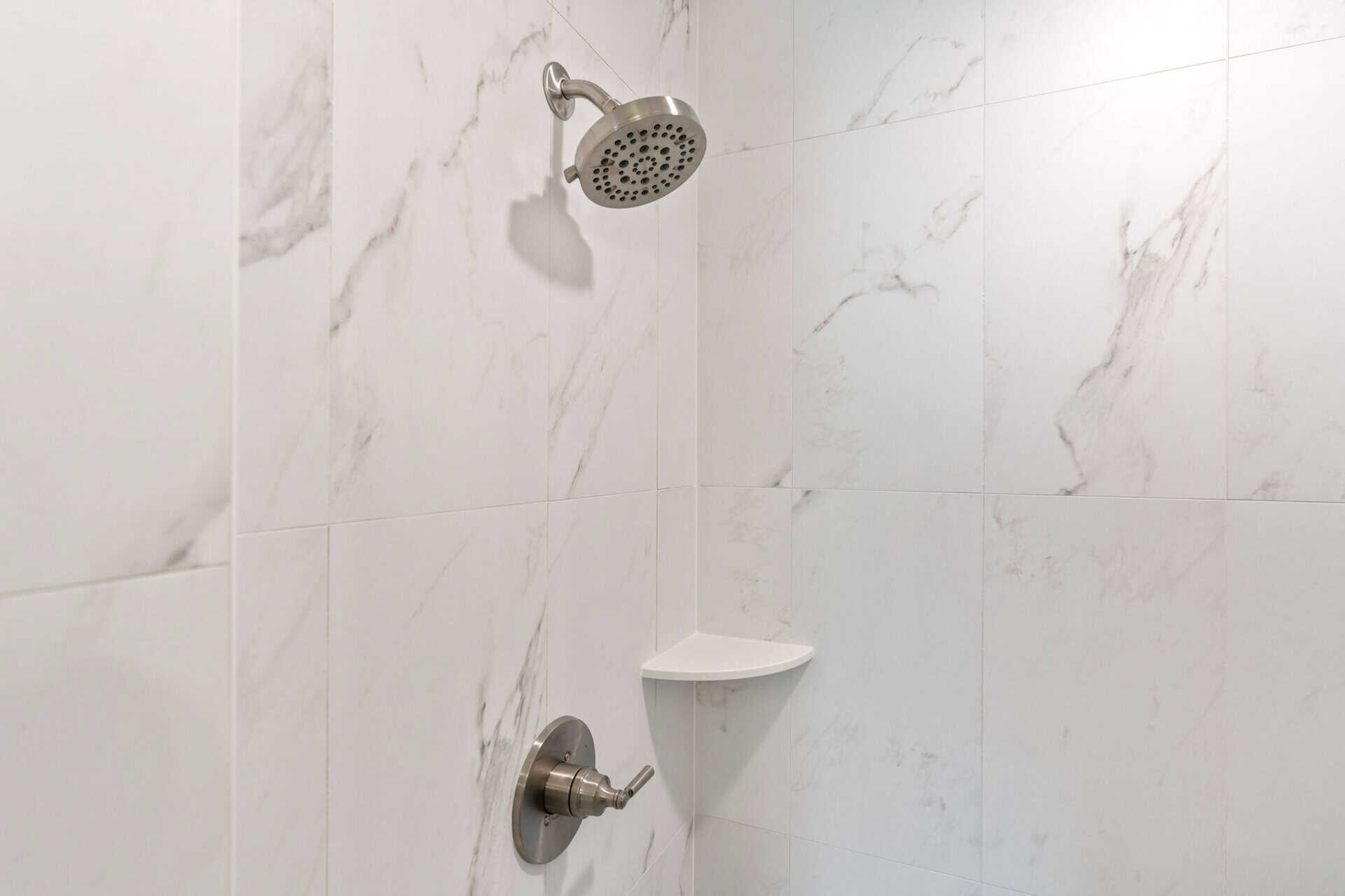 Close-up of a modern shower with marble tiles and a corner shelf.