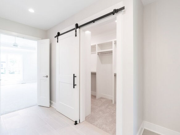 Spacious walk-in closet with white shelves and sliding barn door in modern home.