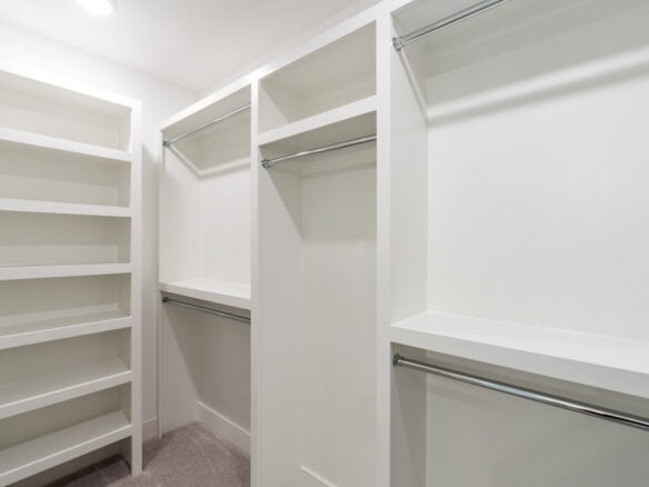 Spacious walk-in closet with white shelves and hanging rods in a new home.