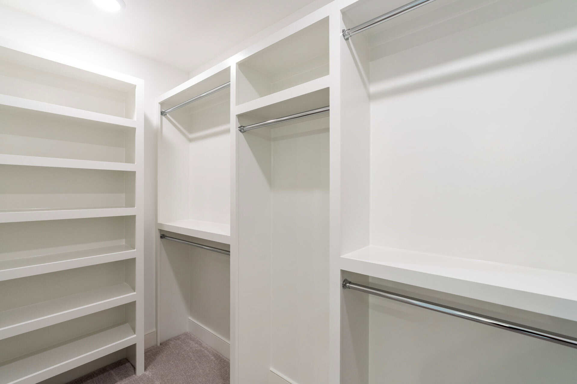Spacious walk-in closet with white shelves and hanging rods in a new home.