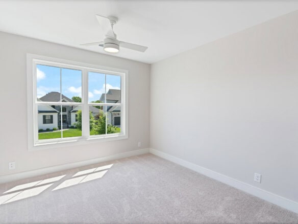 Bright empty room with large window and ceiling fan in a new home.