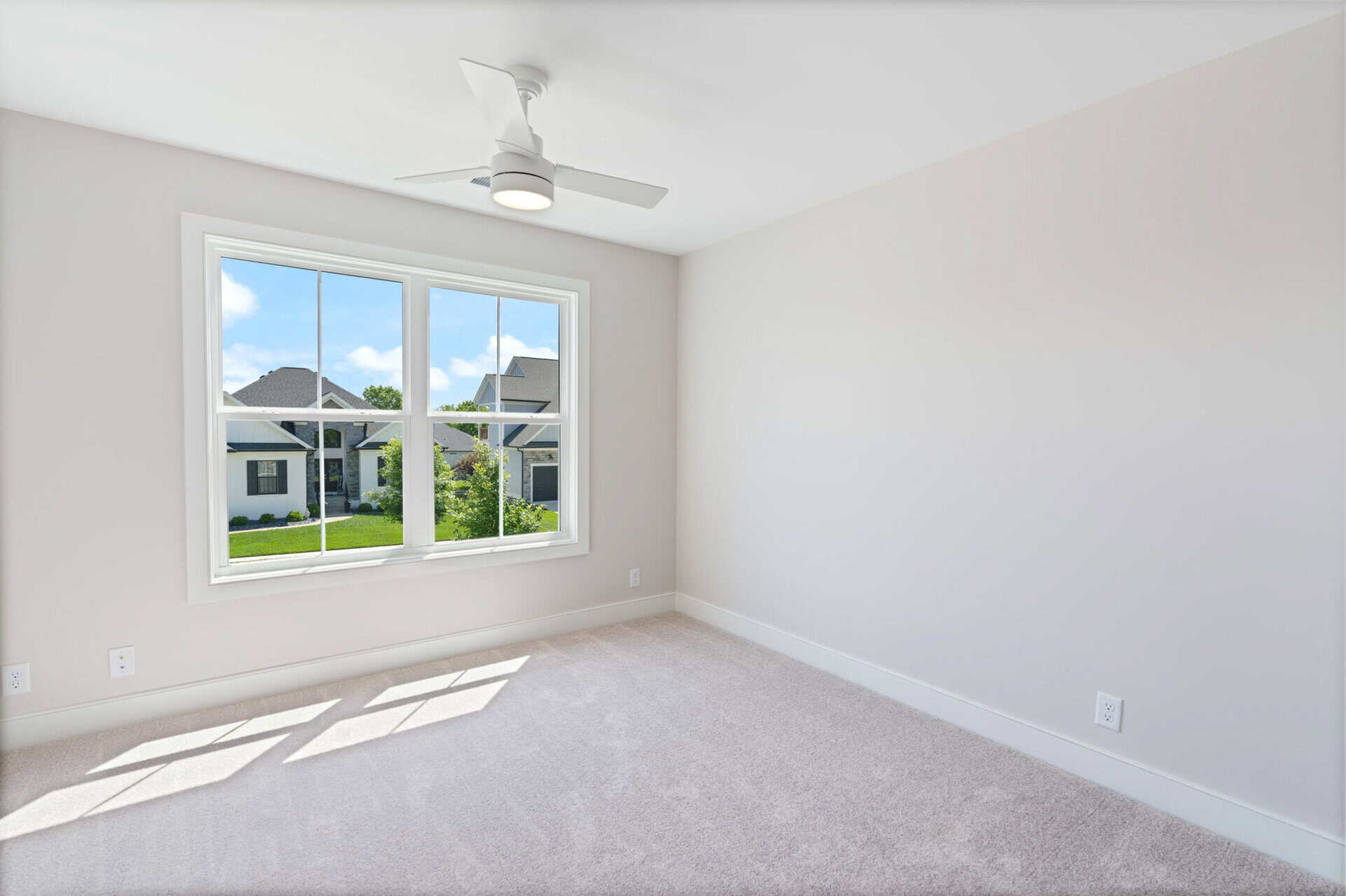 Bright empty room with large window and ceiling fan in a new home.
