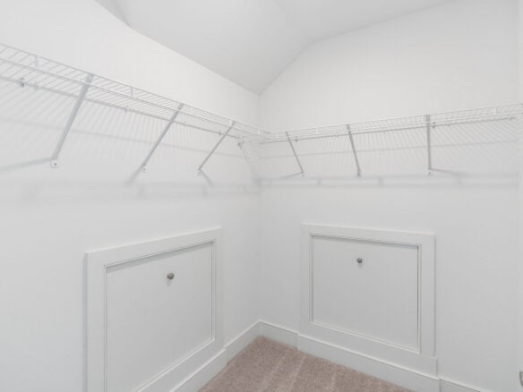 White walk-in closet with metal wire shelving along two walls and built-in lower cabinets; light beige carpet on floor.