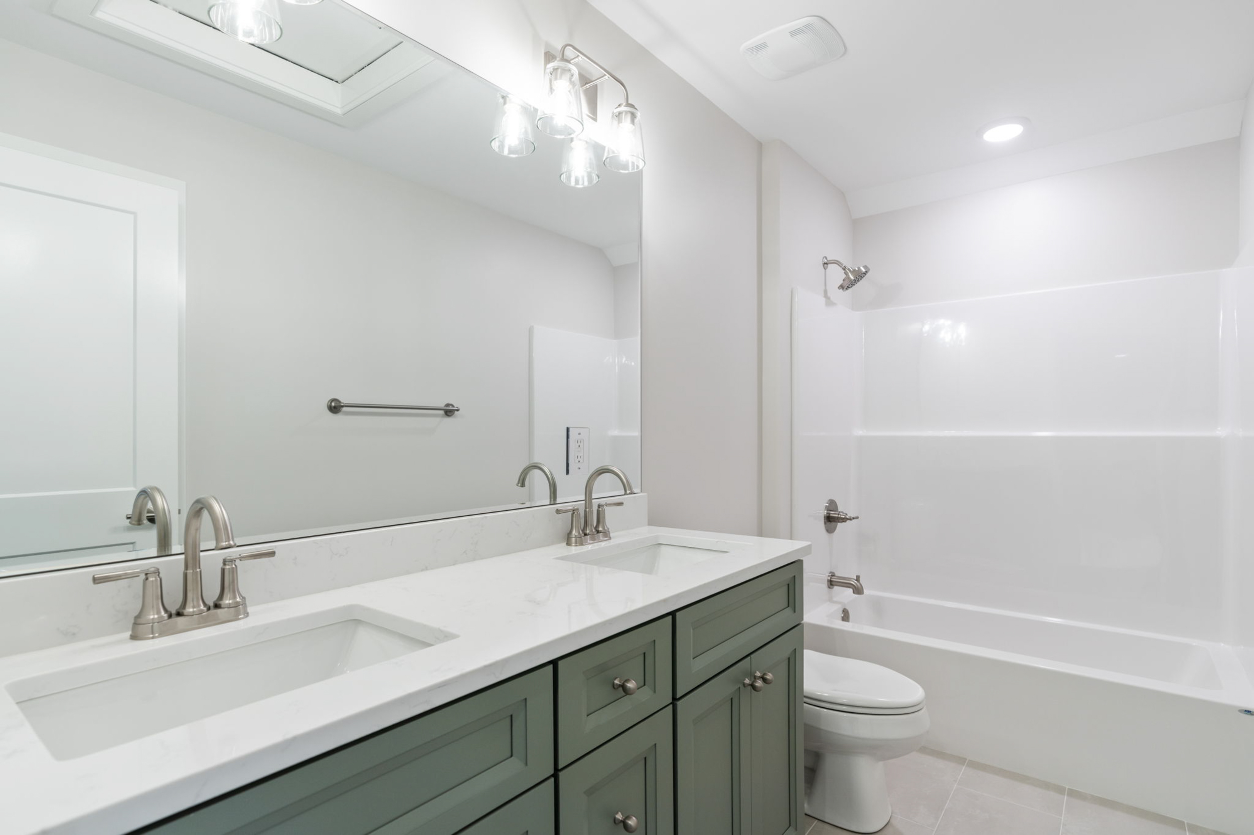 Double-sink bathroom vanity with marble countertop and gray cabinets, large wall mirror, and brushed-nickel fixtures in a bright, modern bathroom.