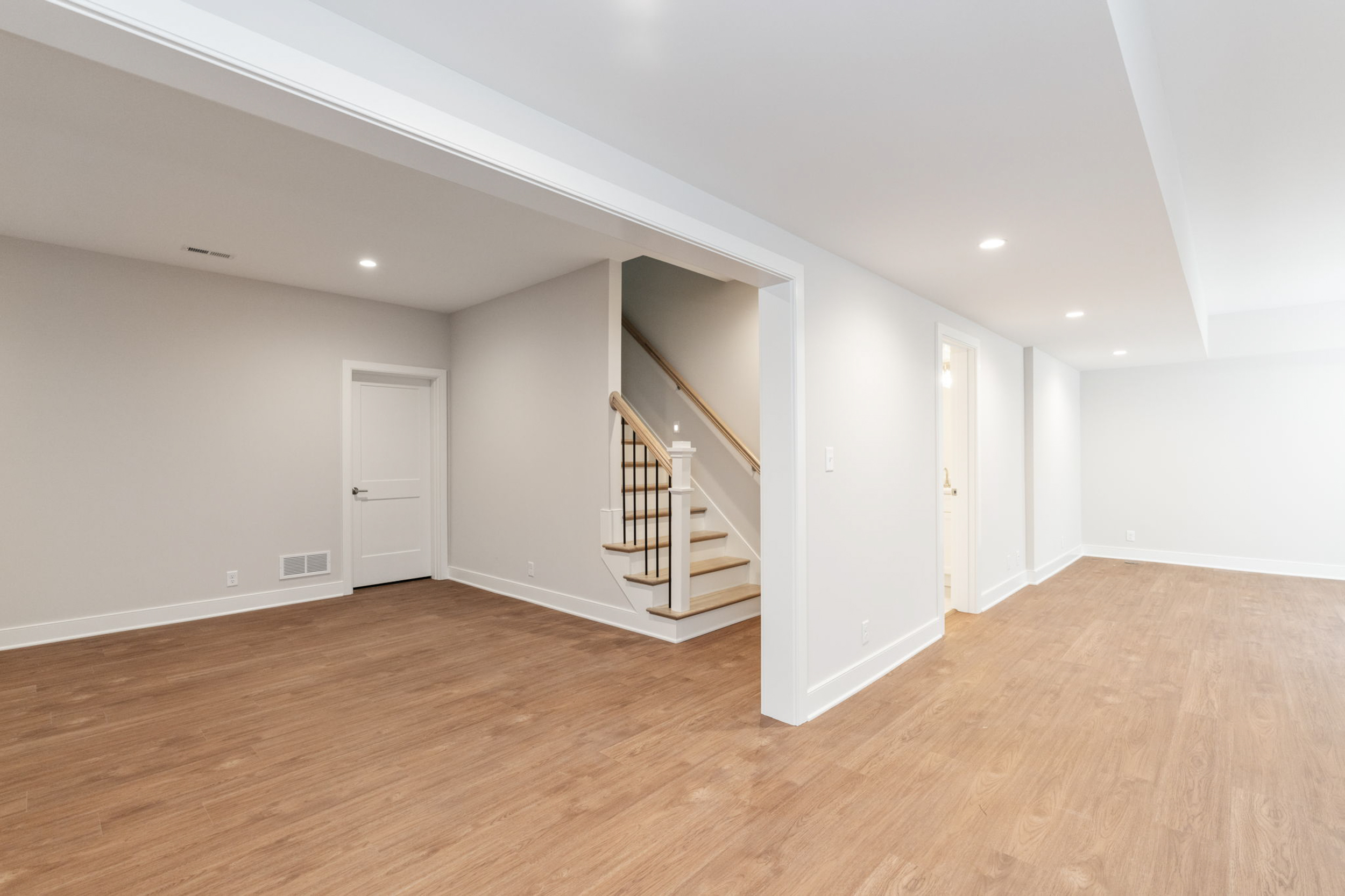 Empty modern basement hallway with stairs on the left, white walls, and recessed ceiling lights.