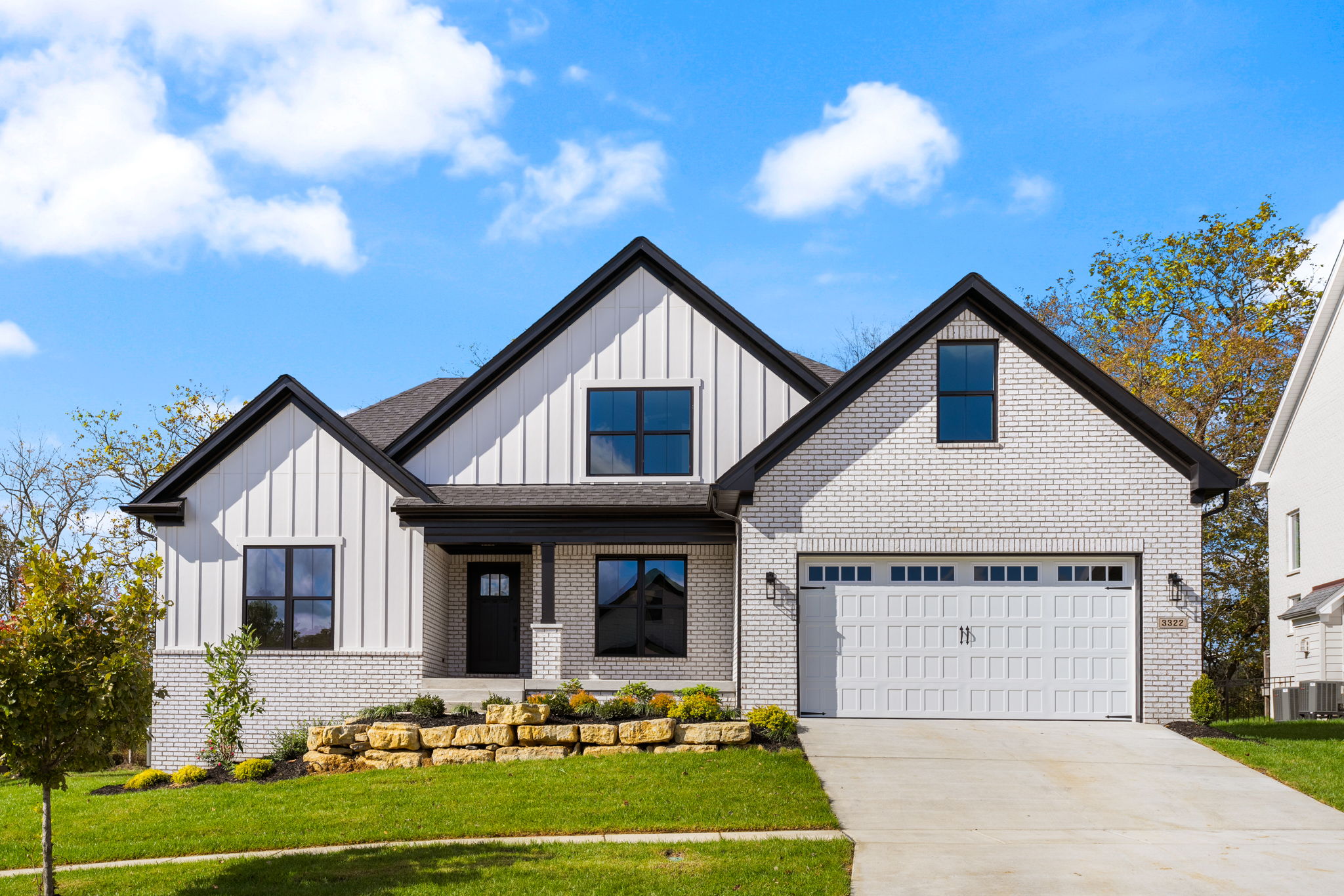3322 Catalpa Farms Dr-1 Modern two-story brick-and-siding house with two peaked roofs, large front windows, and a double garage on a sunny day.