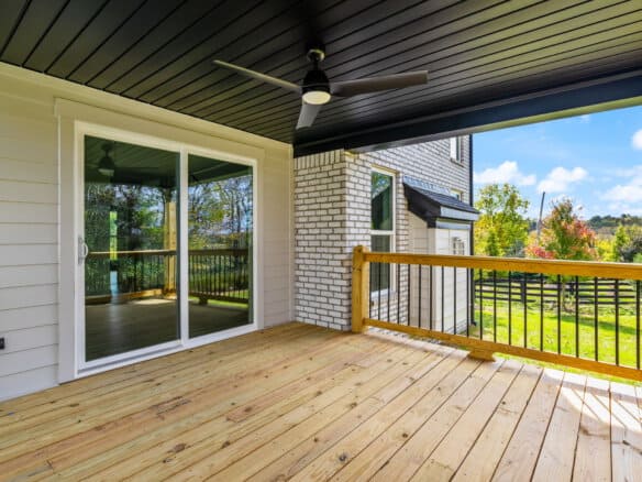 Covered balcony with ceiling fan and scenic view of trees and sky.