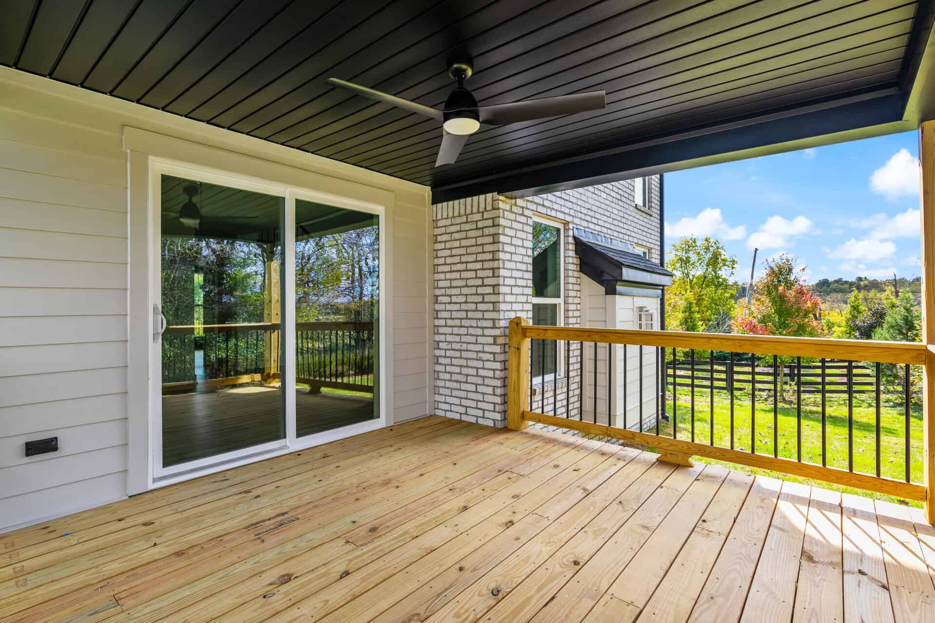 Covered balcony with ceiling fan and scenic view of trees and sky.