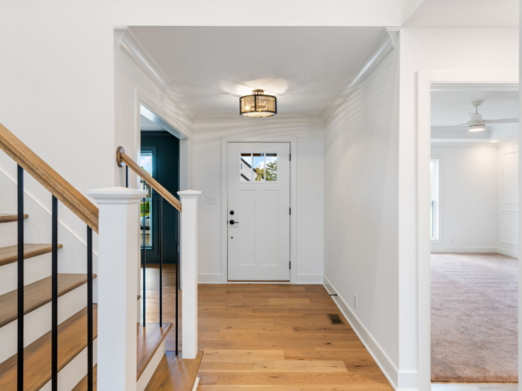 Bright foyer with wood stairs on the left, white walls, and a front door with a window at the end.