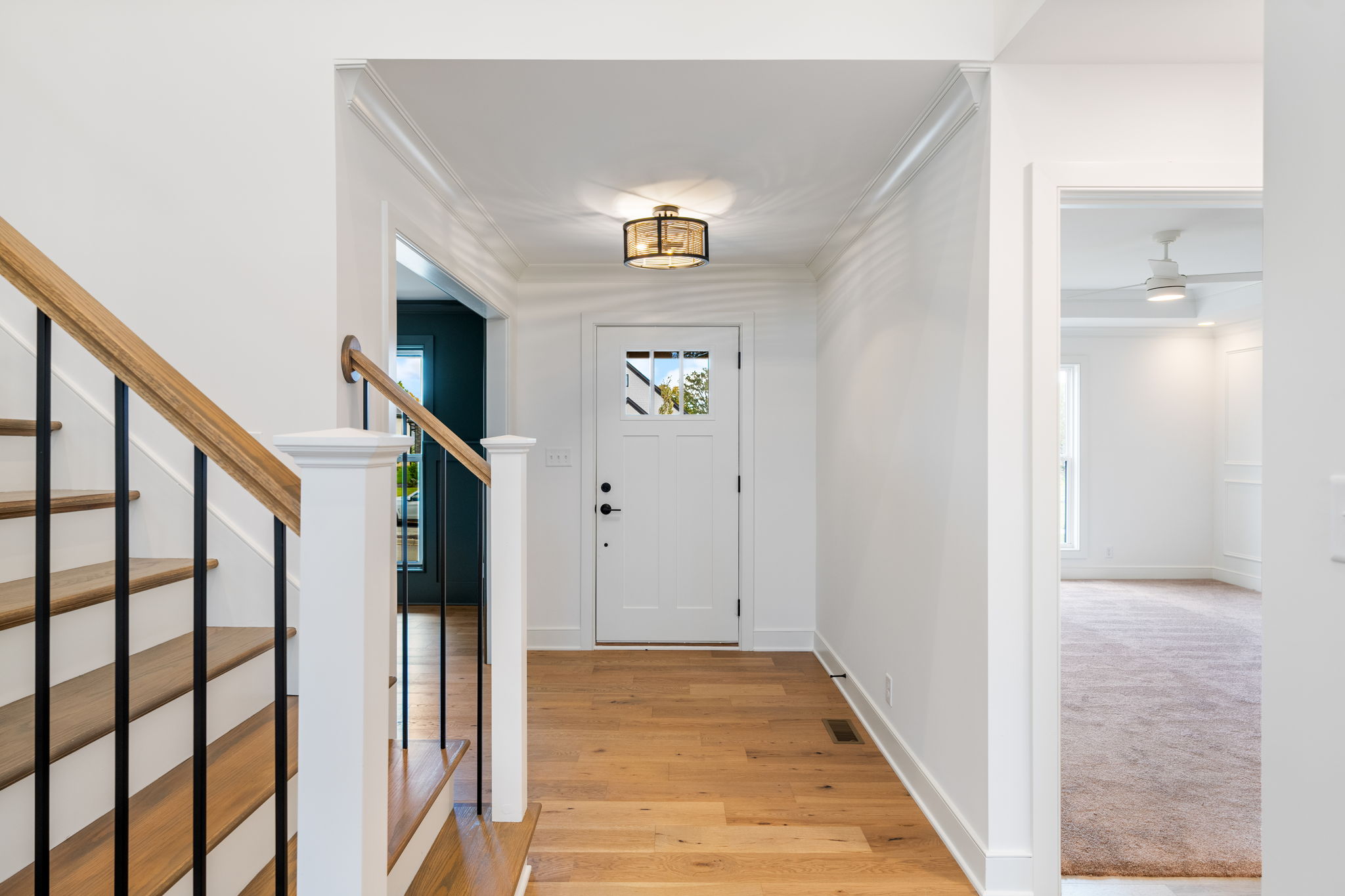 Bright foyer with wood stairs on the left, white walls, and a front door with a window at the end.