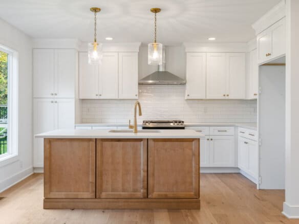 Modern white kitchen with island, pendant lights, and stainless steel range hood.