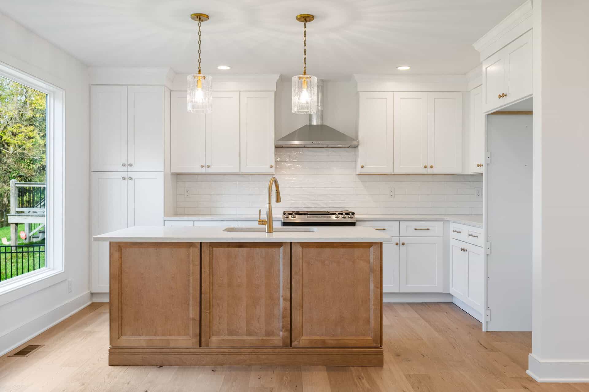 Modern white kitchen with island, pendant lights, and stainless steel range hood.