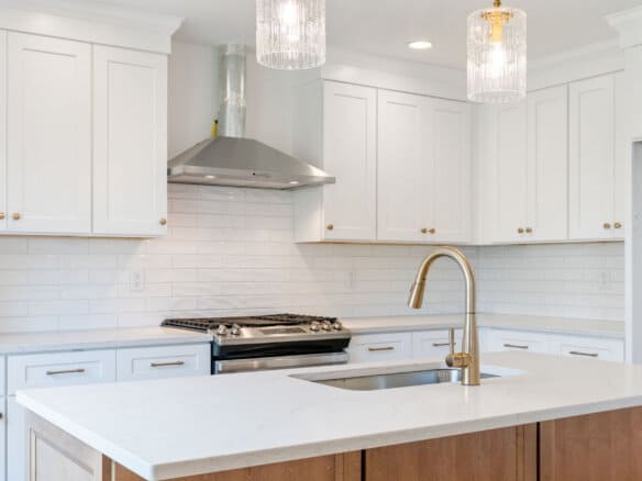 Modern white kitchen with gold fixtures and pendant lighting.