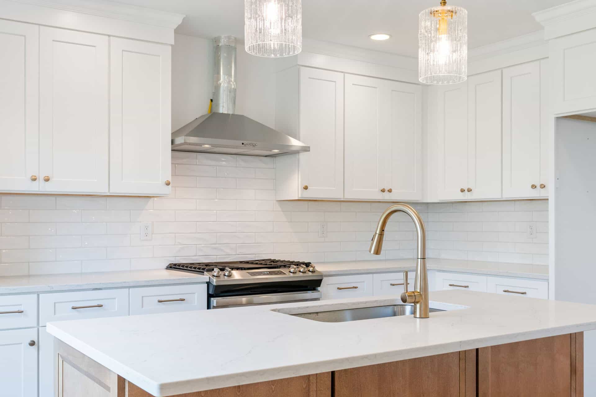 Modern white kitchen with gold fixtures and pendant lighting.