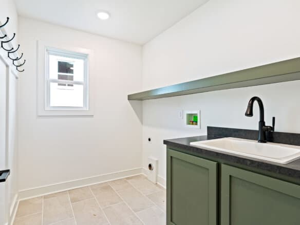 Laundry room with white walls, window, and green cabinetry with black countertop.