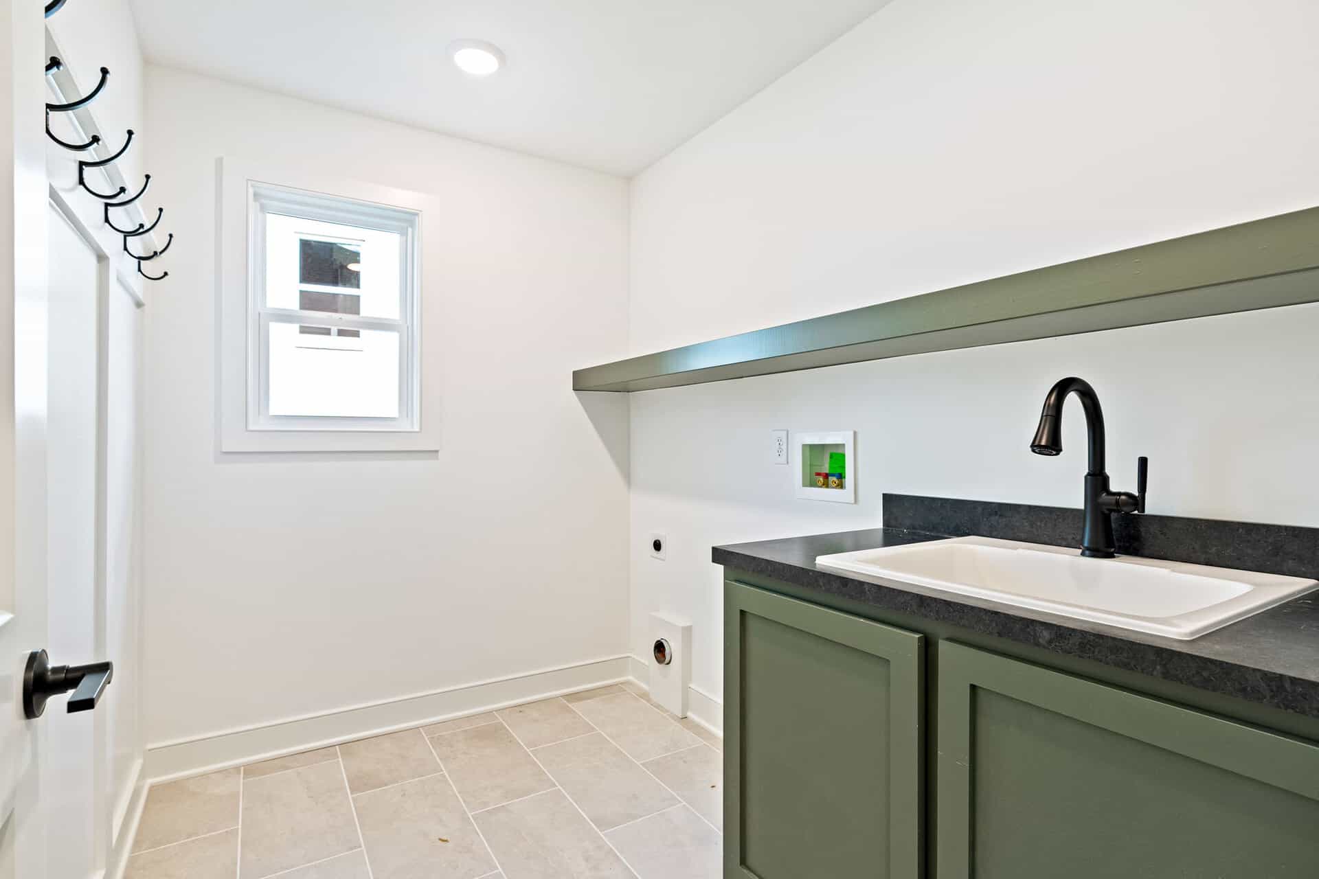 Laundry room with white walls, window, and green cabinetry with black countertop.