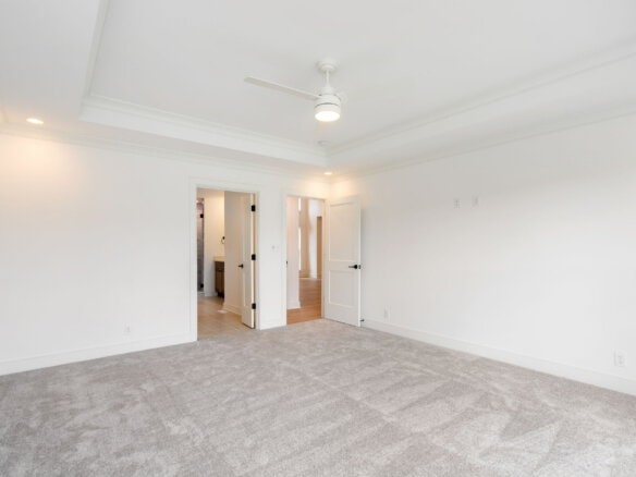 Spacious empty bedroom with white walls, ceiling fan, and gray carpet.