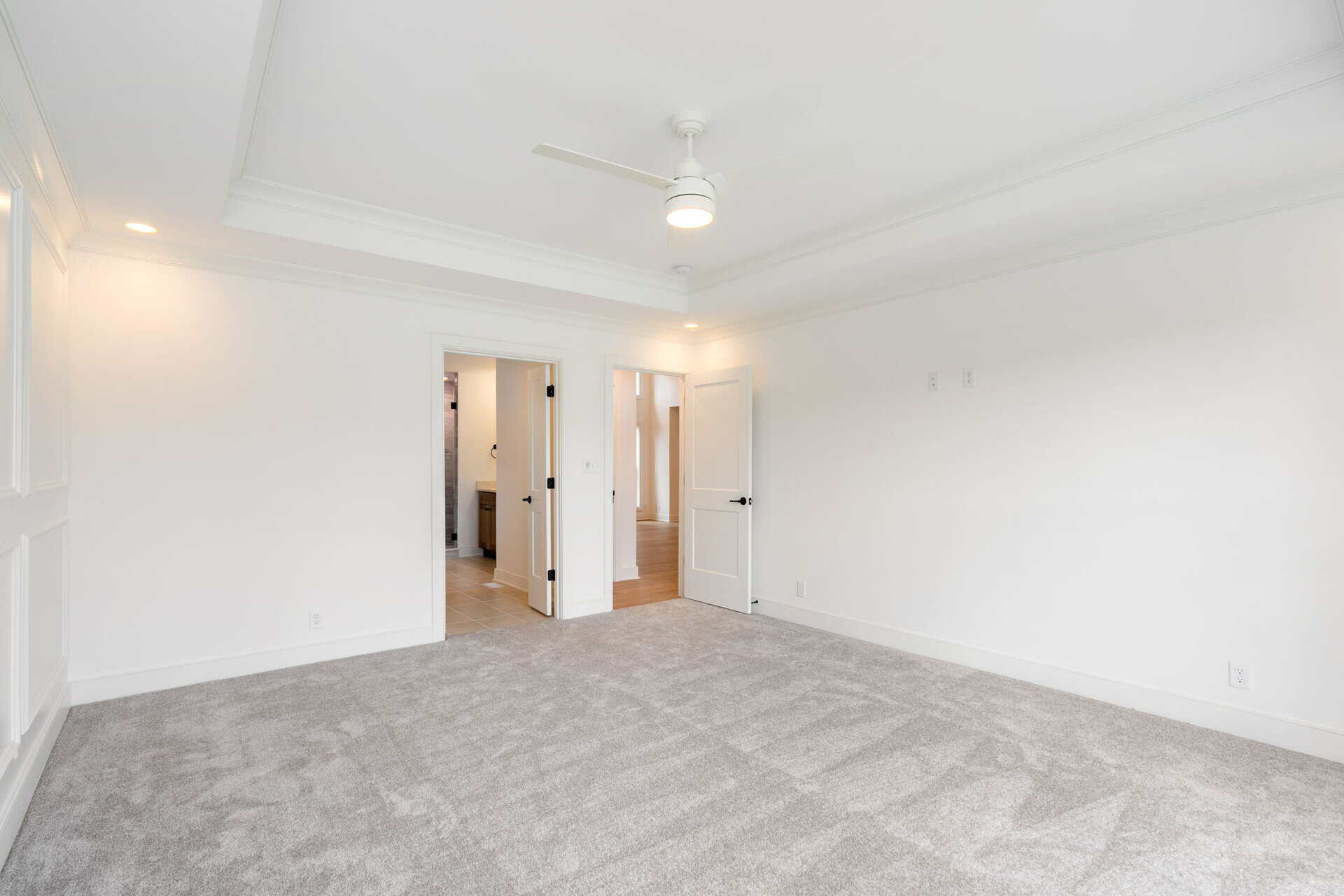 Spacious empty bedroom with white walls, ceiling fan, and gray carpet.