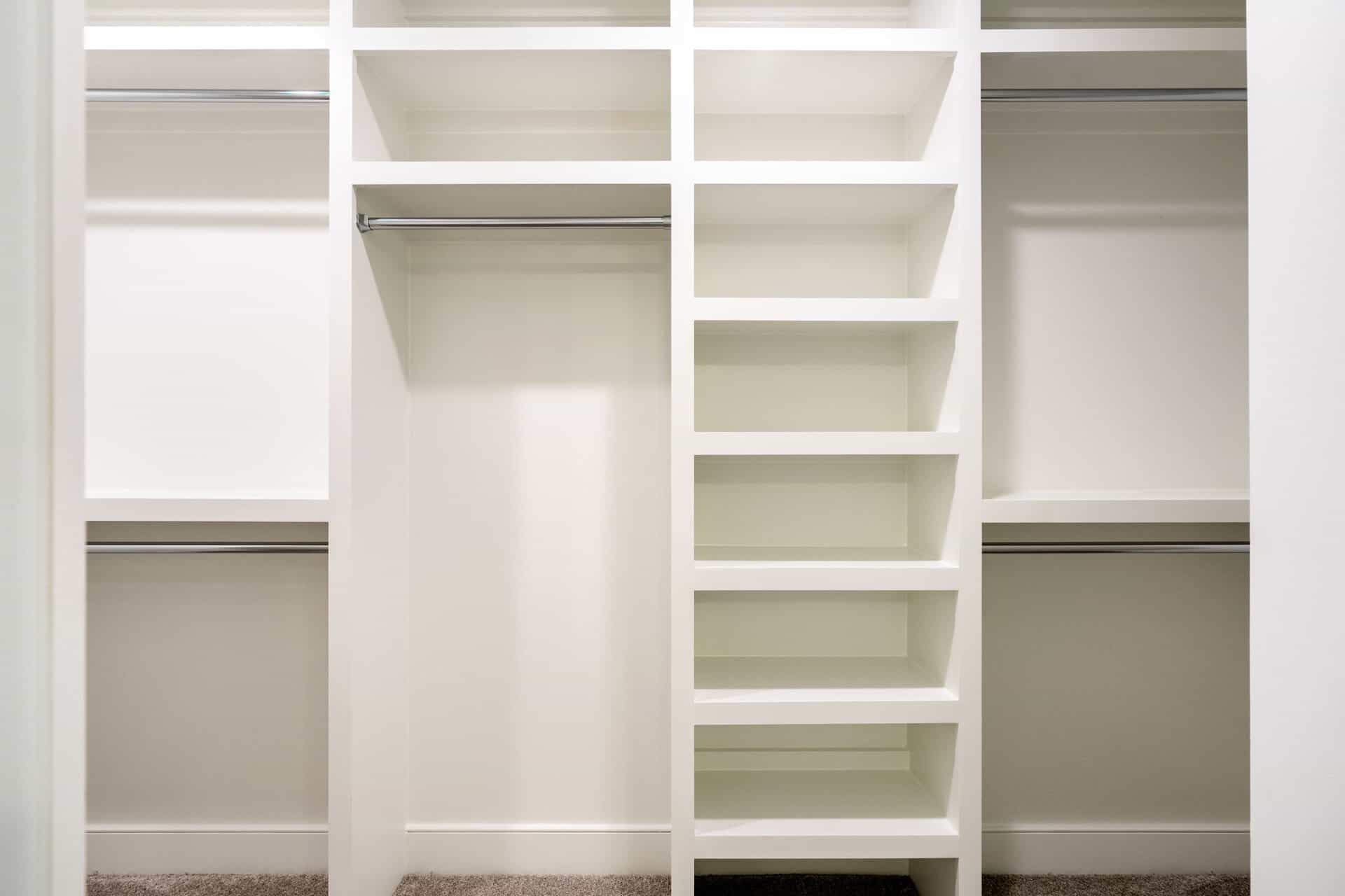 Empty white walk-in closet with shelves and hanging rods.