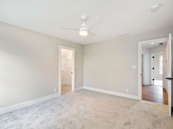 Empty bedroom with beige carpet, white walls, and ceiling fan.