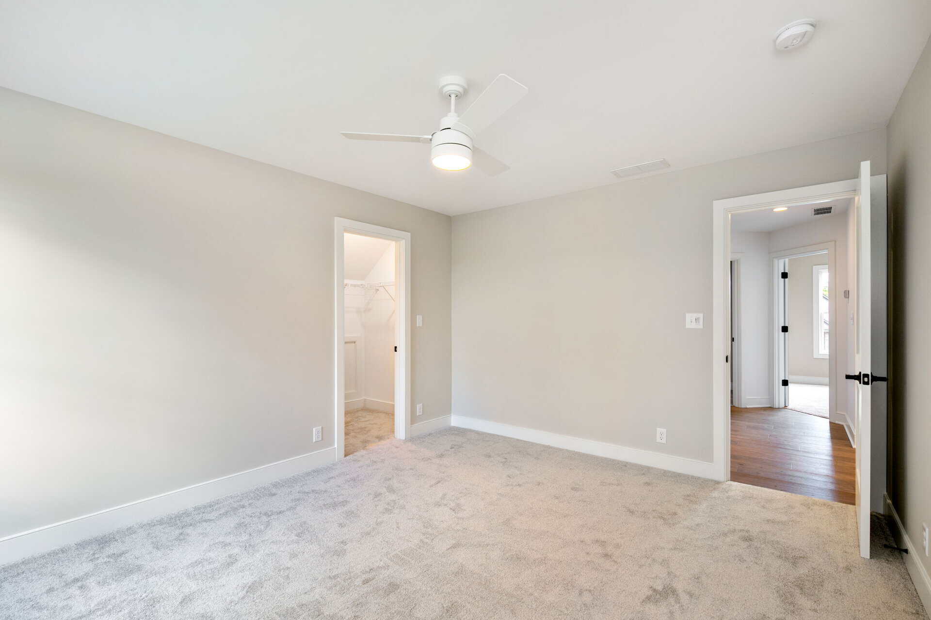 Empty bedroom with beige carpet, white walls, and ceiling fan.