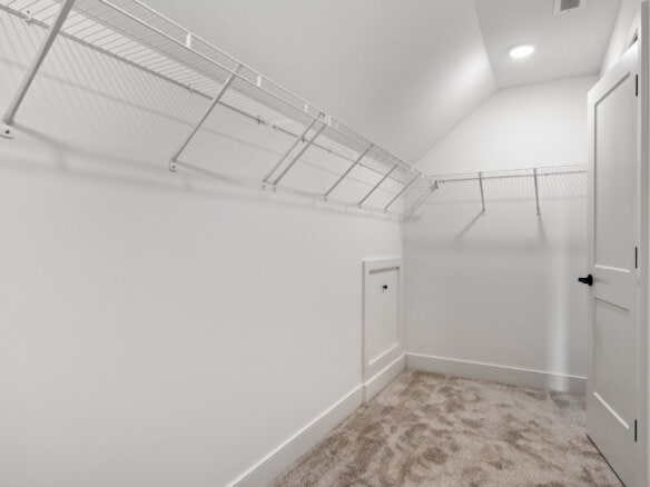 Empty walk-in closet with white walls, wire shelving, and beige carpet.