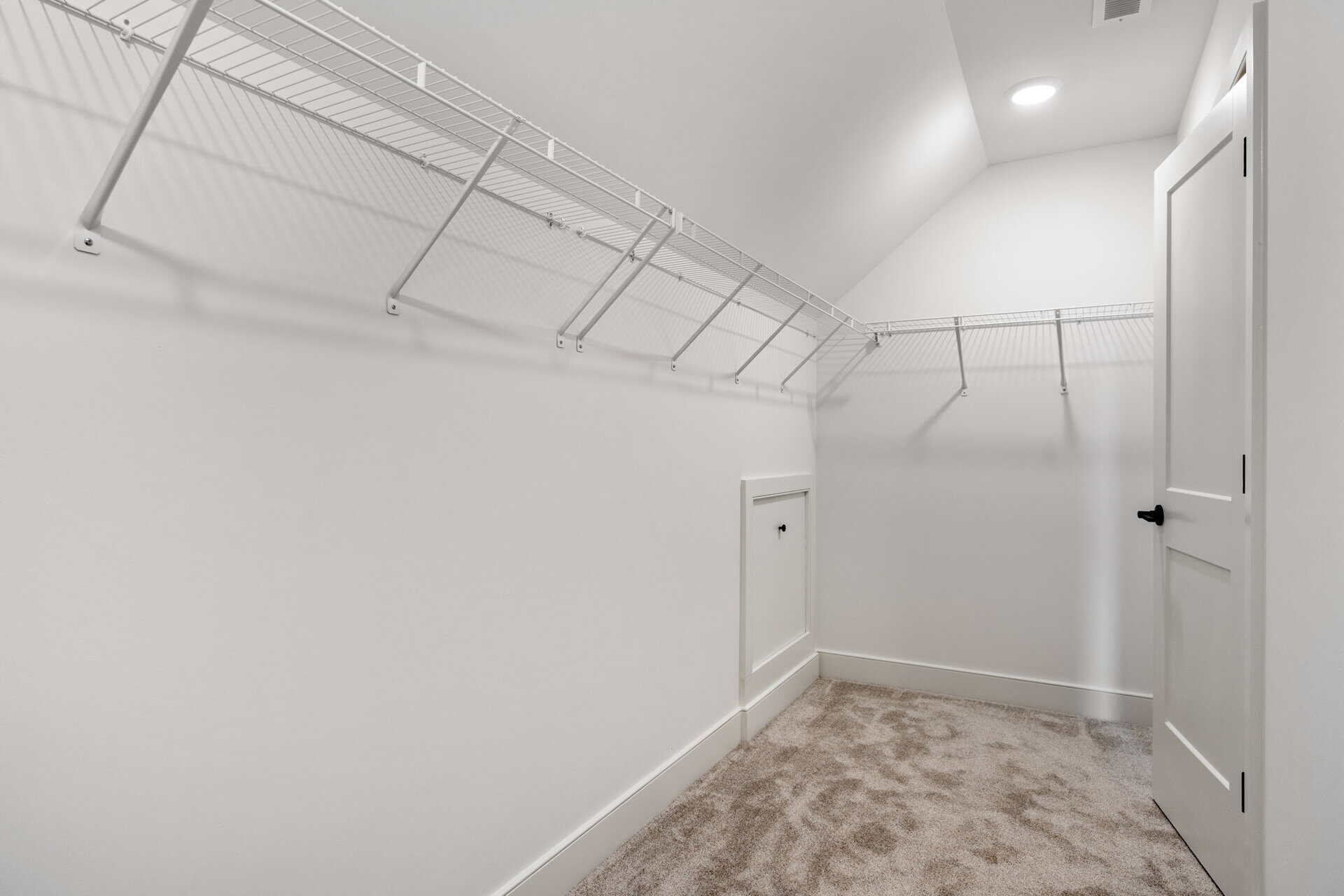 Empty walk-in closet with white walls, wire shelving, and beige carpet.