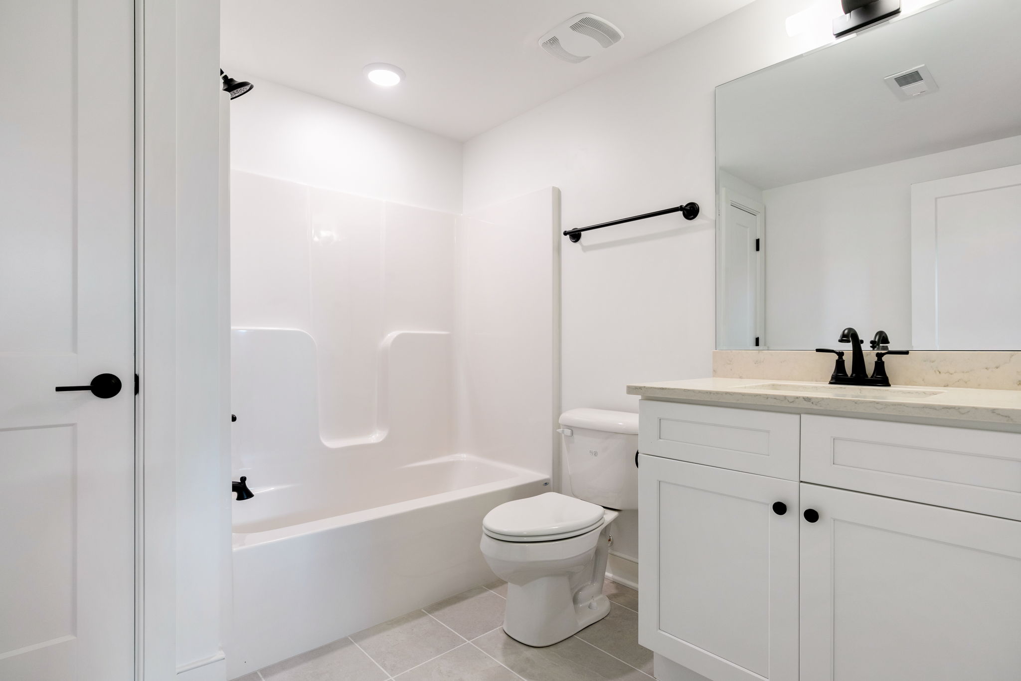 White bathroom with a tub/shower, black fixtures, and a marble countertop vanity with a large mirror above it.