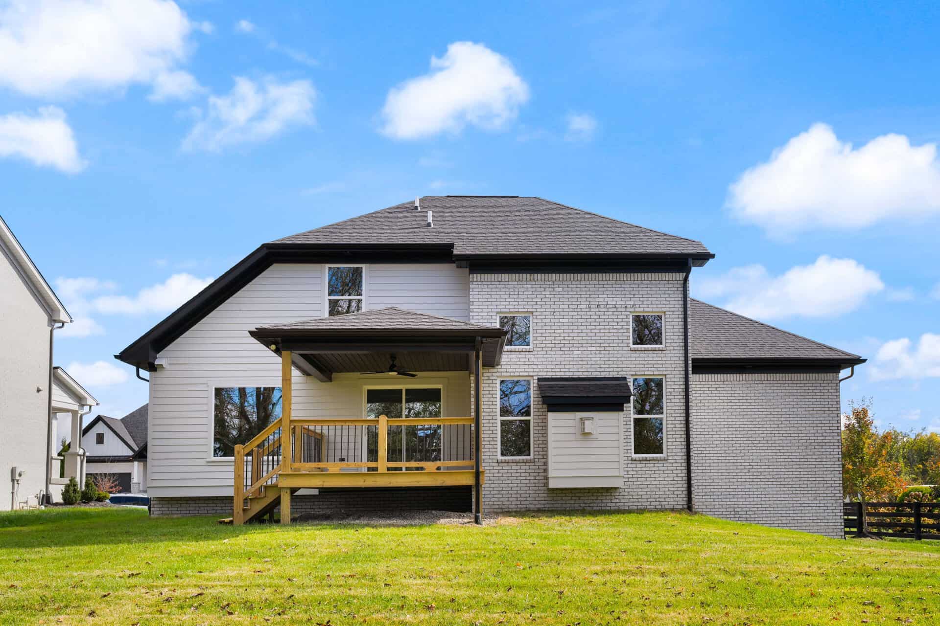Modern two-story house with a wooden deck and gray brick exterior.