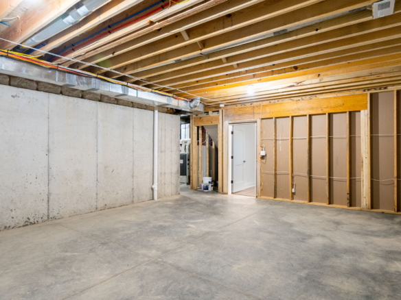 Unfinished basement with exposed joists, concrete walls, and visible wiring; doorway to a back room in renovation area.
