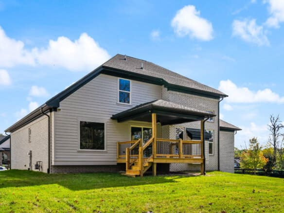 Modern two-story house with a wooden deck and green lawn under a blue sky.