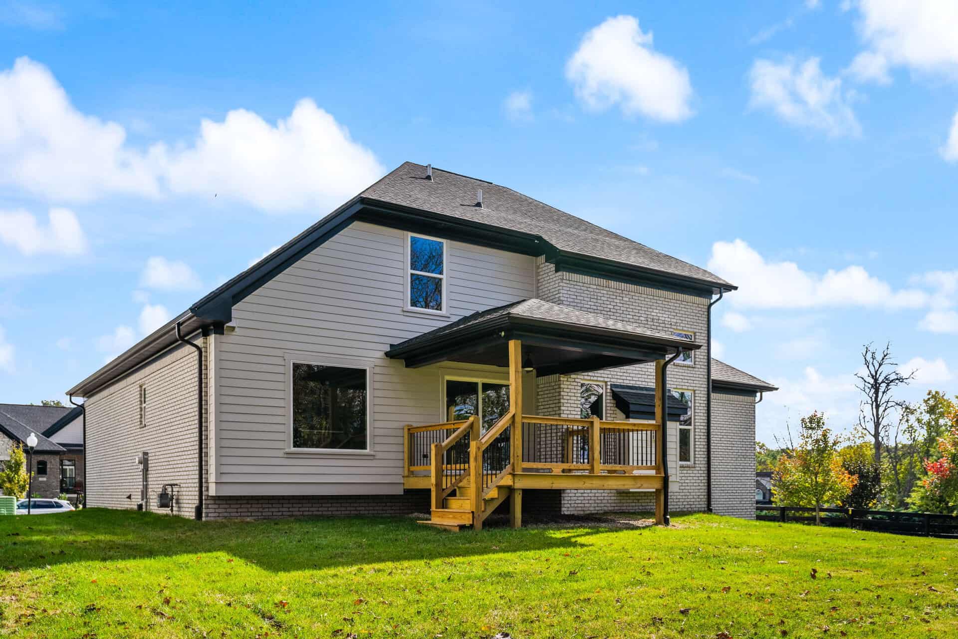 Modern two-story house with a wooden deck and green lawn under a blue sky.