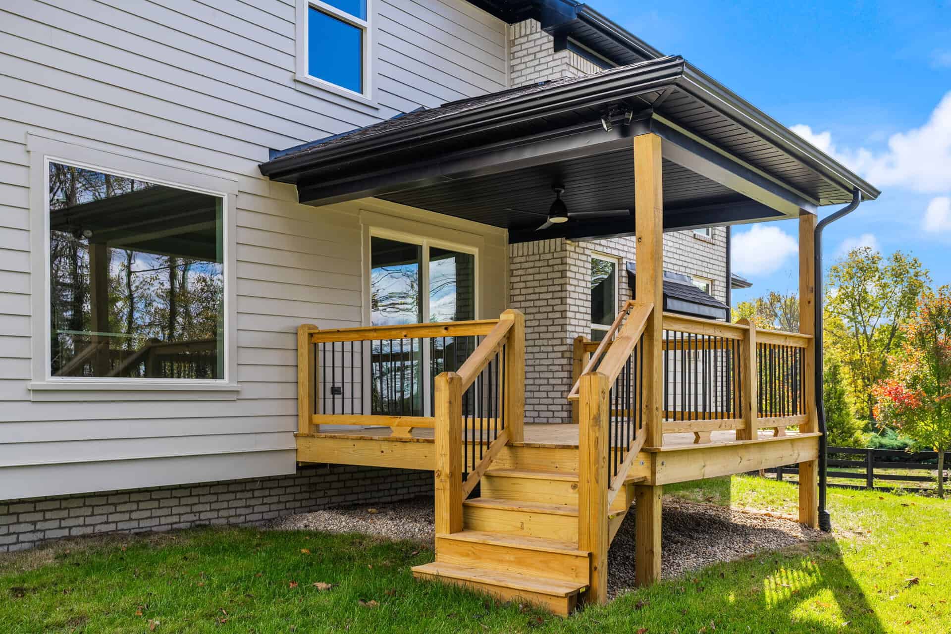 Newly built wooden deck with stairs and black ceiling fan in backyard.
