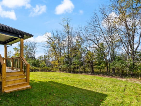 Spacious backyard with green grass, trees, and a wooden deck in Louisville, KY.